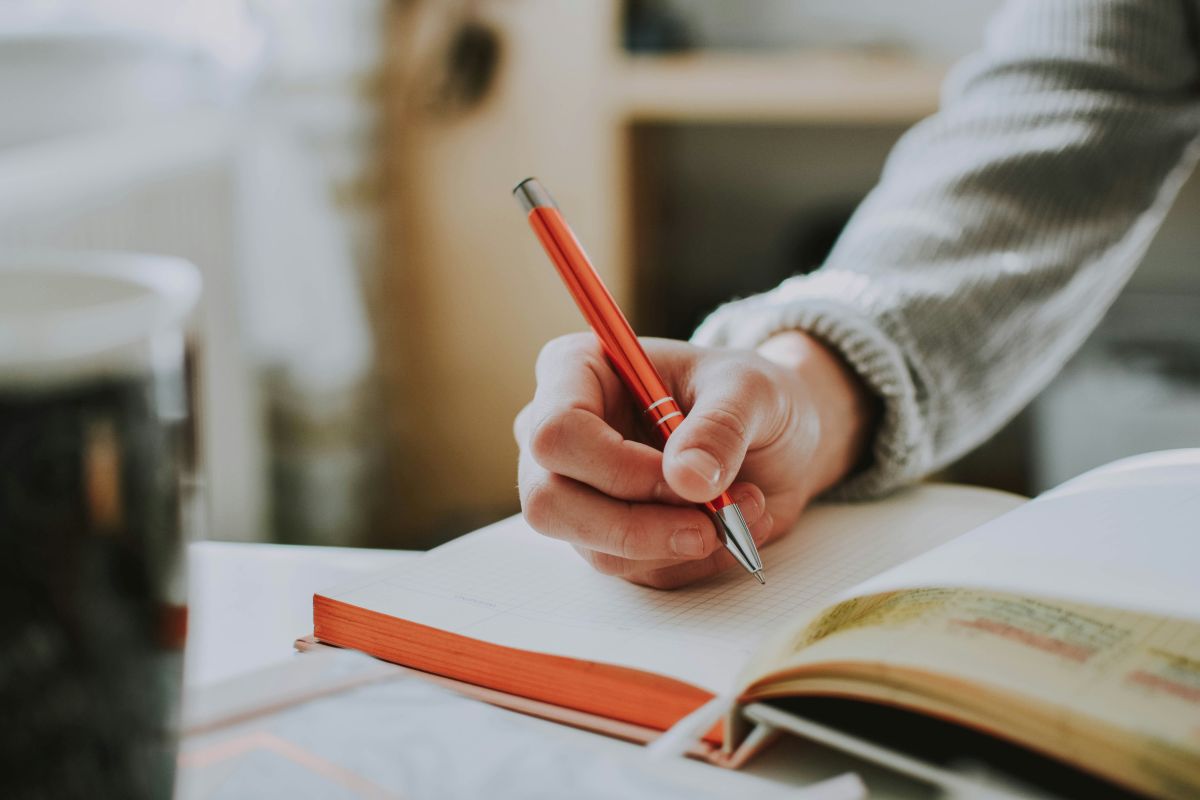 A student’s arm and hand is seen writing on a notebook, using a pen, as part of her experience learning a second language.